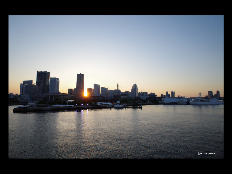 横浜港からランドマークタワーなどのビル群と夕陽を撮影した写真