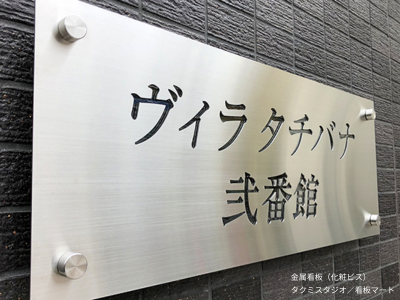 化粧ビスで壁面に取り付けた金属看板。取り付け部分を美しく見せるアクセント付きサイン。