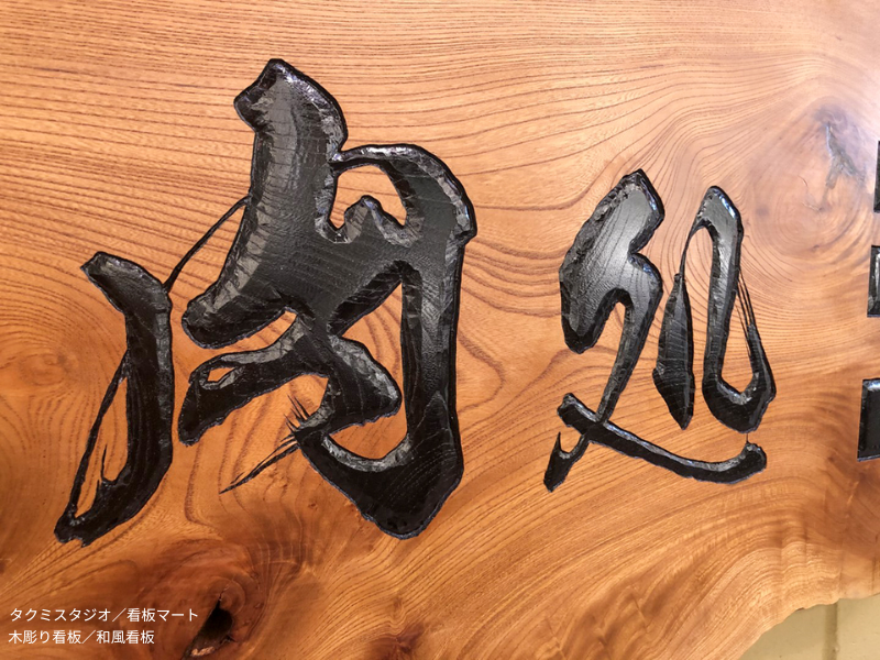 伝統技法で手彫りされた木製看板。温かみと重厚感を兼ね備え、店舗の顔として存在感を放つ。