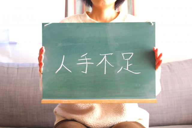 人手不足と書いた黒板文字を持つ女性