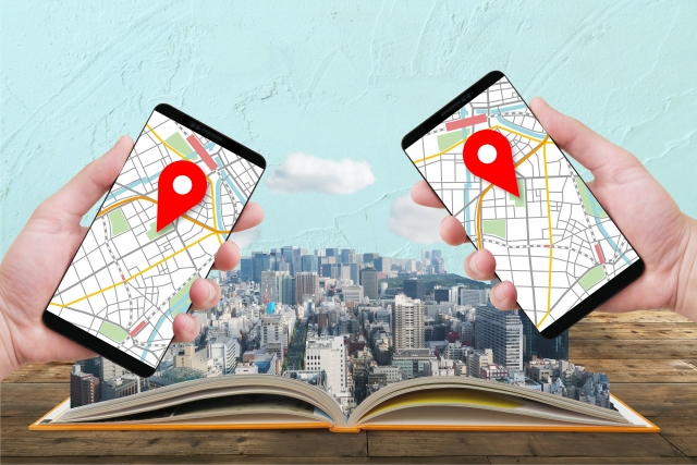スマホで地図情報アプリを表示する二人の手と街並みを表示する本
