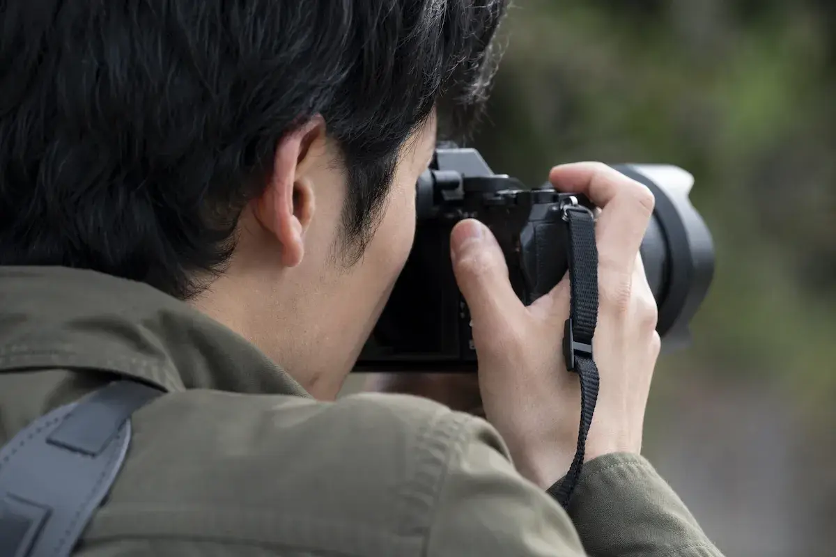 ミラーレスカメラのファインダーを覗いている日本人男性の姿。 斜め後ろから、肩越しにアップで。