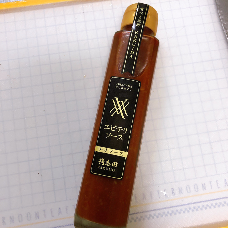 白地のまな板の上に細長い瓶に入ったエビチリソース。ラベルには「食べる黒酢KAKUIDA エビチリソース」という黒字に金文字のラベルが貼ってある