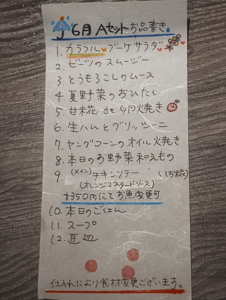 手書きの「6月Aセット」メニュー。色鉛筆で飾られた紙に、季節の野菜やチキンソテーなどの料理名が書かれている。
