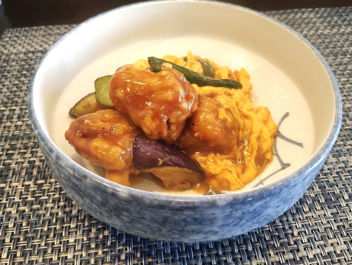 とろみのあるソースが絡んだ鶏肉の唐揚げ、ふわふわの炒り卵、ナスやなどの野菜が深皿に盛り付けられた料理