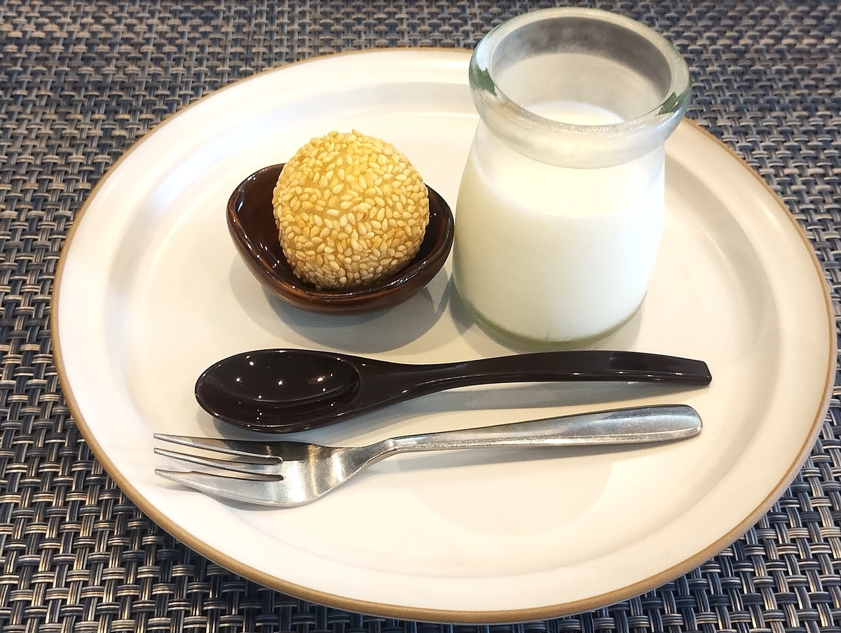 小さな器に盛られた丸いごま団子と、ガラス瓶に入った白い杏仁豆腐が、黒いスプーンやフォークと一緒に白い丸皿に載せられたデザートセット