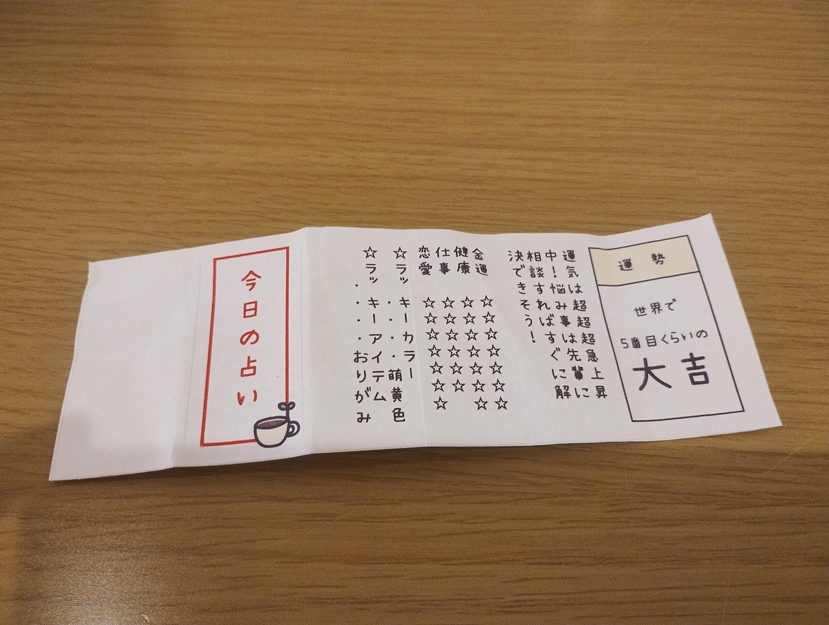 はこにわ珈琲で引いた「今日の占い」の紙。木のテーブルに置かれた大吉のおみくじ。世界で５番目くらいの大吉と書かれている。