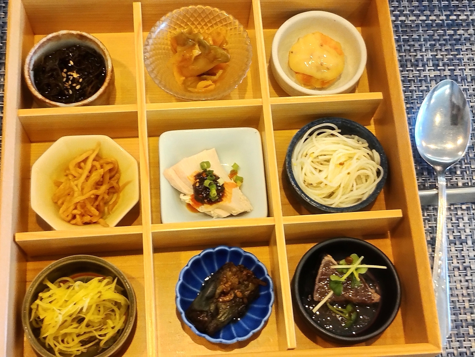 九つの小鉢に盛られた和食の前菜盛り合わせ。もずく、豆腐、そうめんなどが木箱に並ぶ