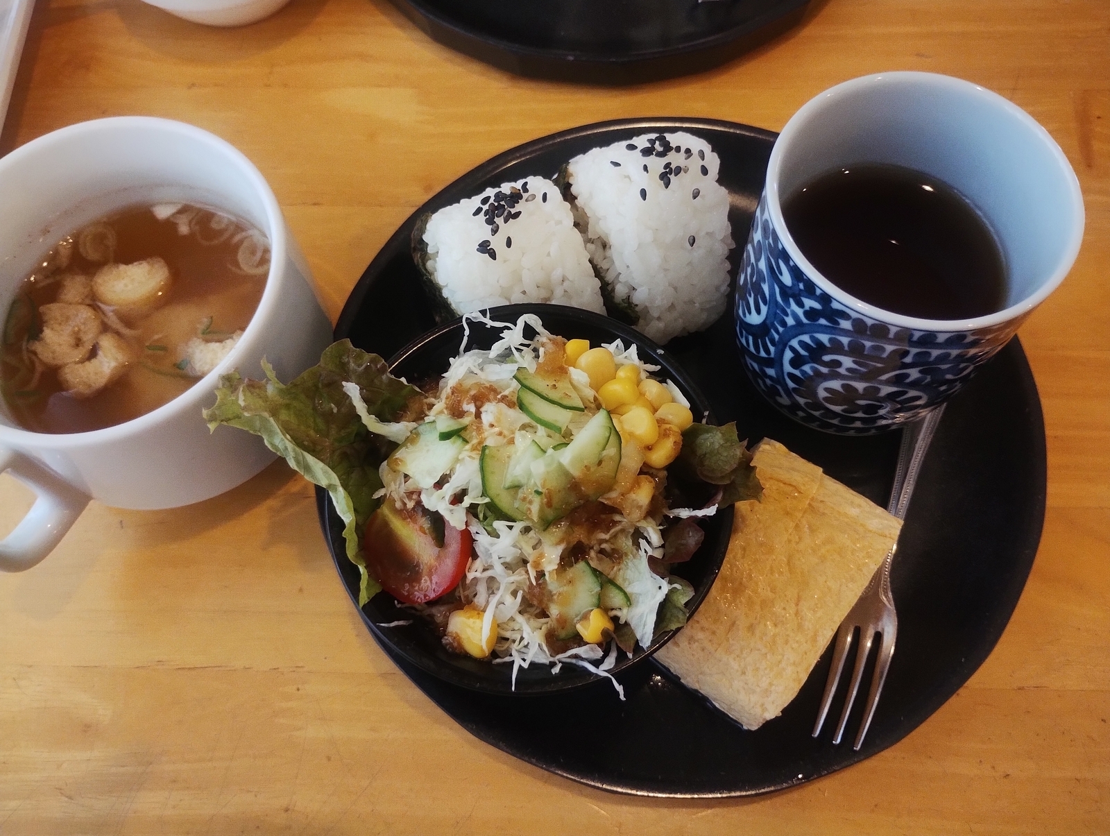 黒い皿に盛られたおにぎり、サラダ、卵焼き、味噌汁、そして湯飲みの日本の朝食セット