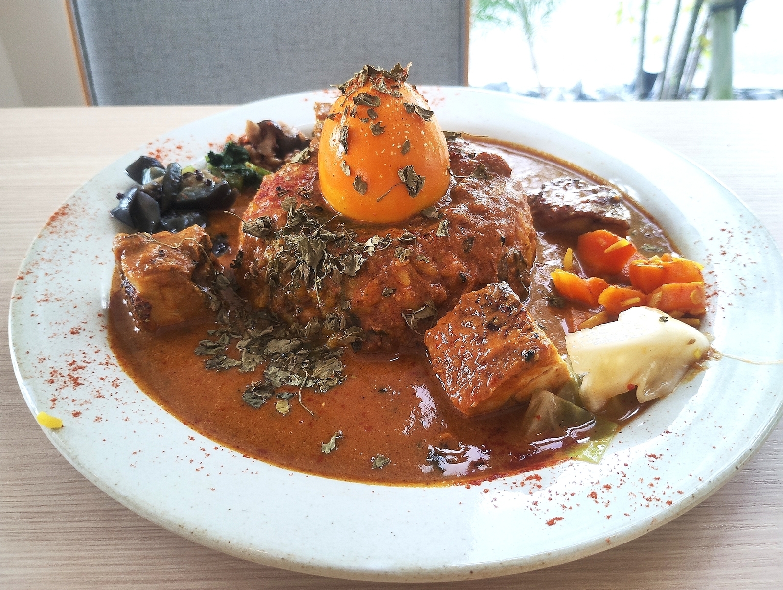 親子チキンカレーのプレート。中央に卵黄をのせたハンバーグ風ライス、周囲に野菜と肉が盛られた濃厚ソース