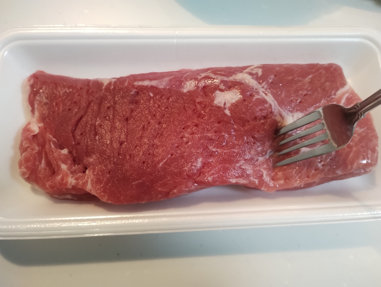 フォークで下ごしらえ中の豚肩ロース肉、味が染みやすくなるように穴をあけているところ