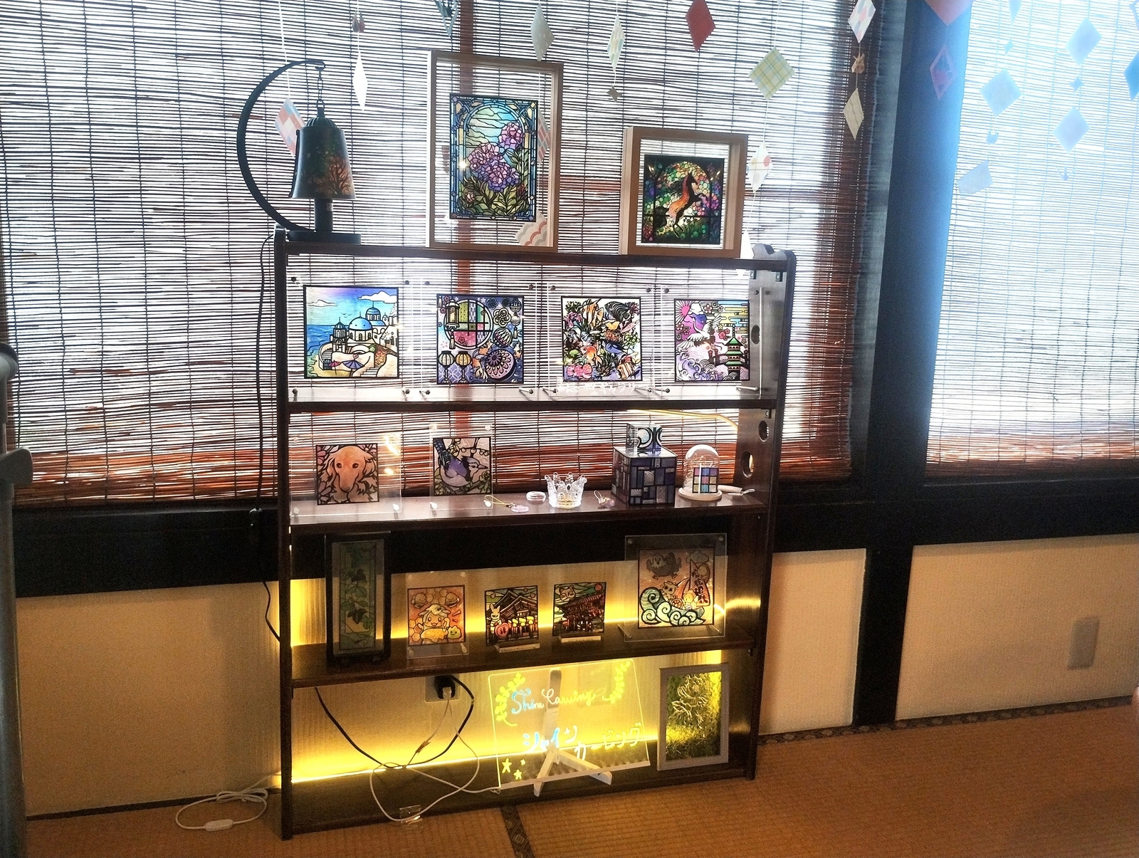 岐阜県関市「恩田ギャラリー」店内の展示棚。竹のすだれ越しに光が差し込み、棚には色とりどりのステンドグラス作品が並ぶ。花や風景、動物などのモチーフが飾られ、古民家カフェらしい落ち着いた雰囲気。