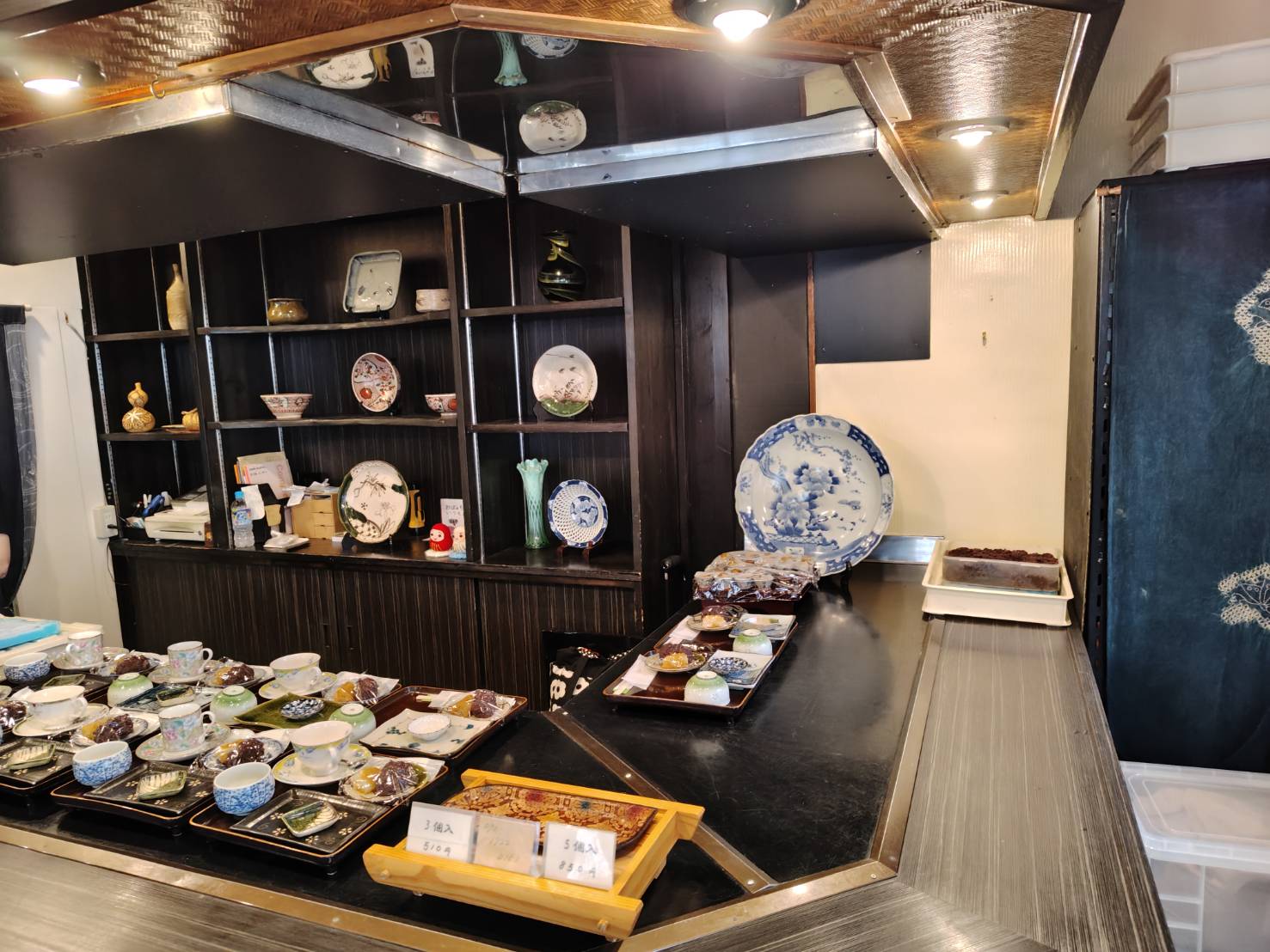 和菓子とティーセットが並ぶ店内カウンター。奥には陶器の器が並び、上品で静かな雰囲気が漂う