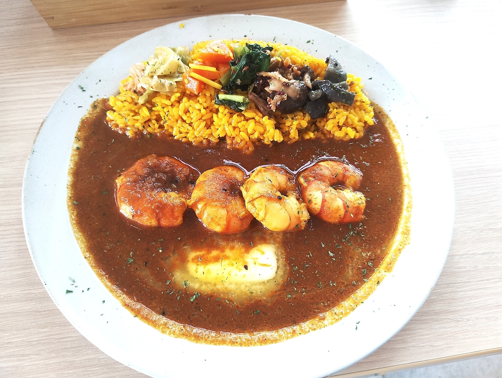 海老が並ぶスパイスカレーと黄色いライスのプレート。野菜のトッピング付き。