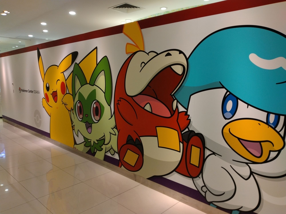 壁に大きく「Pokémon Center OSAKA」の文字と、左からピカチュウ・ニャオハ・ホゲータ・クワッスのイラストが描かれている壁の写真