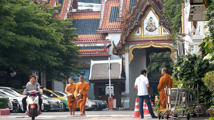 バンコクにある駐車場を歩く僧侶とバイクで通り過ぎる女性たち