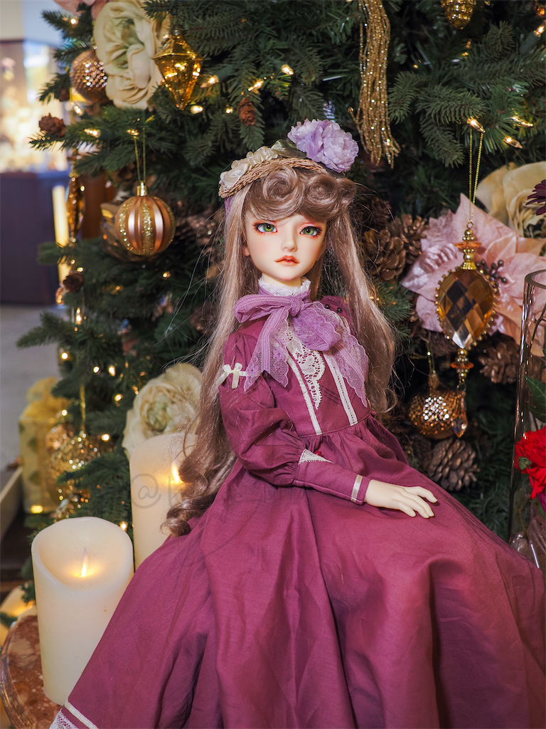 クリスマスツリーを背景にプラムピンクのドレスを着たつかさくんの写真