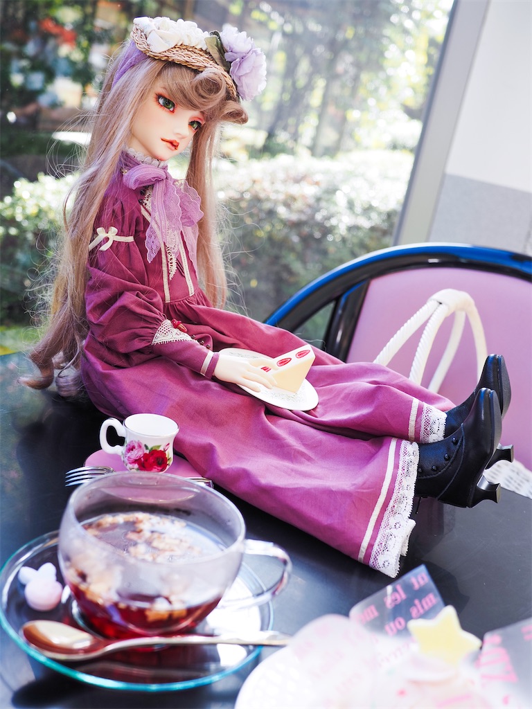 喫茶室でフルーツティーとケーキと共に写っているつかさくんの写真。プラムピンクのドレスを着て座っている。
