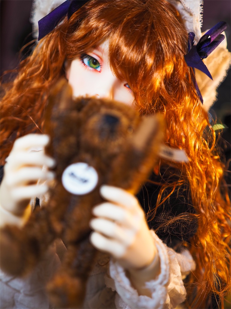 黒いドレスを着た赤毛のつかさくんがテディベアを両手で持って顔の前に持ってきている写真。