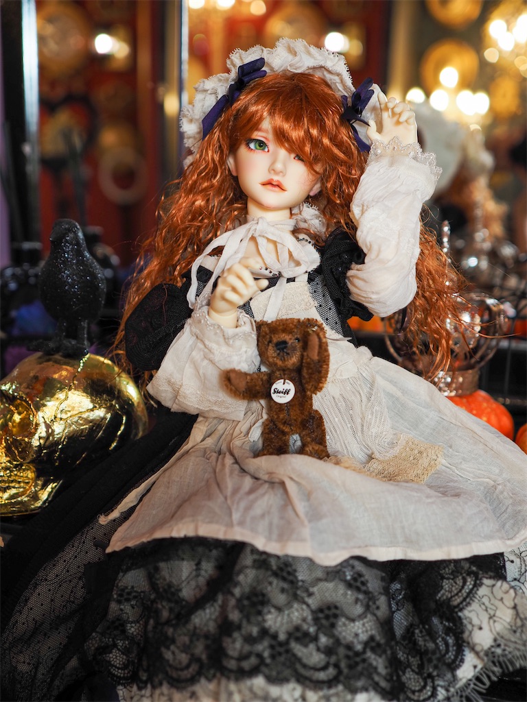 テディベアを膝に載せて脅かすようなポーズを一緒に取っている、黒いドレスを着た赤毛のつかさくんの写真。