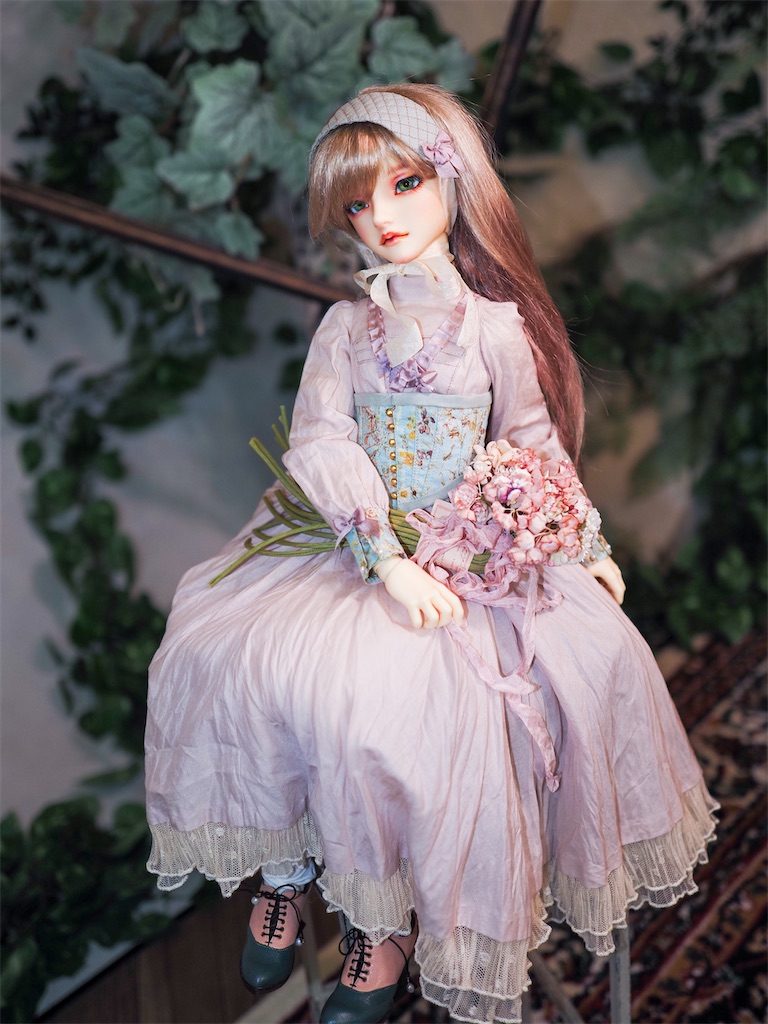 アンティークな雰囲気のグリーンに囲まれて、ピンクの花束を持ってつかさくんが座っている写真。