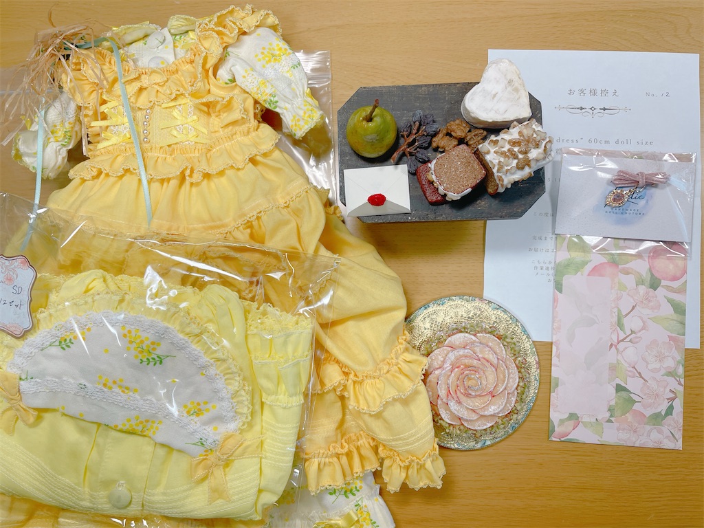 黄色いドレス、リンゴのタルト、チーズやケーキや洋梨のフェイクフード、お客様控えの紙やノベルティが机の上に広げられている写真。