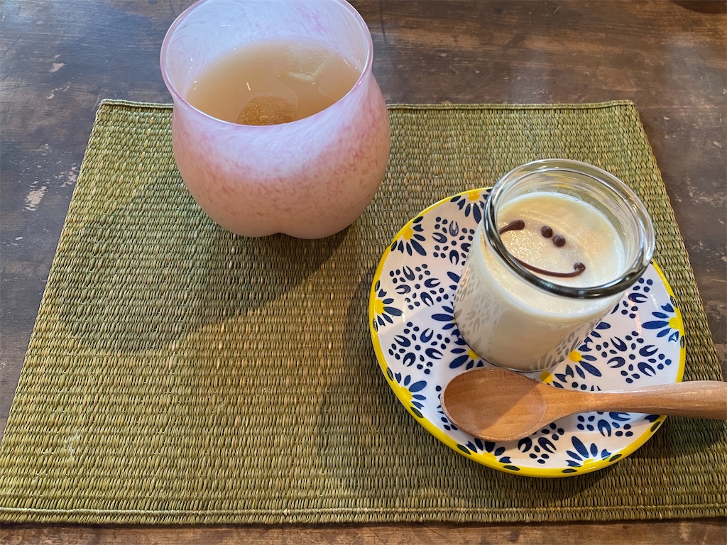 桃色で底がお尻のようになったグラスと笑顔がチョコで描かれたプリンの写真。