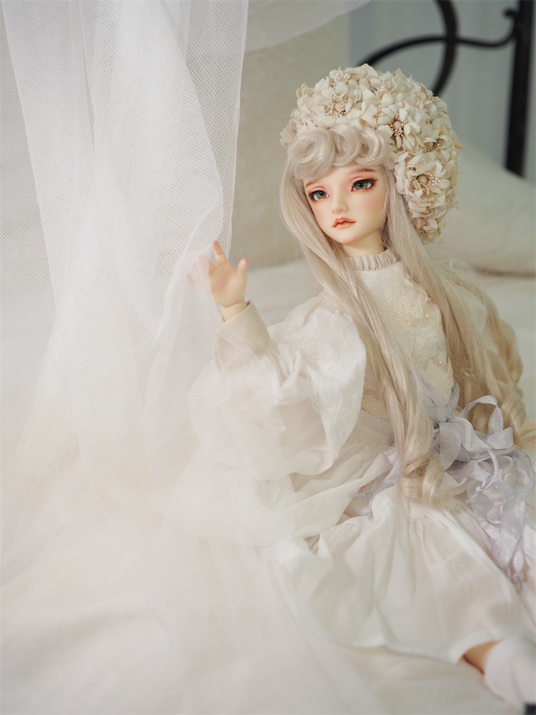 白いドレスを着てエクリュのベレー帽を被り、白いヴェールのカーテンに右手を伸ばしているつかさくんの写真。