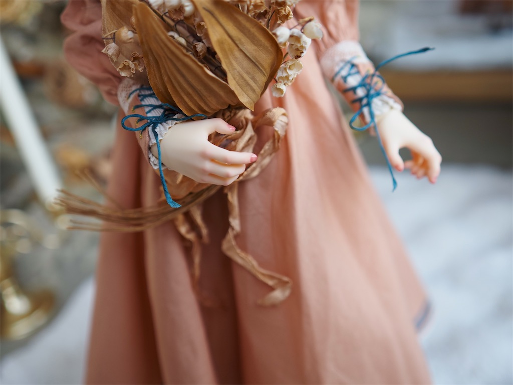 テラコッタオレンジのドレスを着たつかさくんの手元の写真。枯れた鈴蘭の花束を持つ手にピンクのメイクが施されている。
