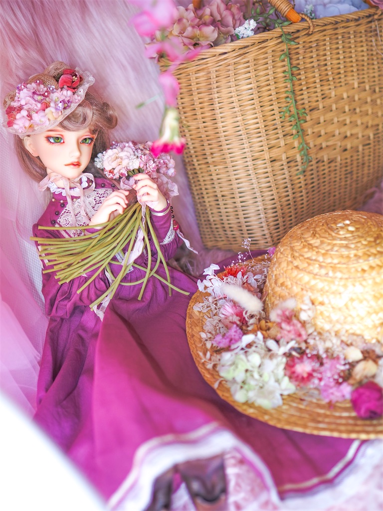 ピンクの花束を持つつかさくんの写真。プラムピンクのドレスを着て、ふわふわしたブランコに腰かけている。花で彩られたカゴや帽子が置かれている。
