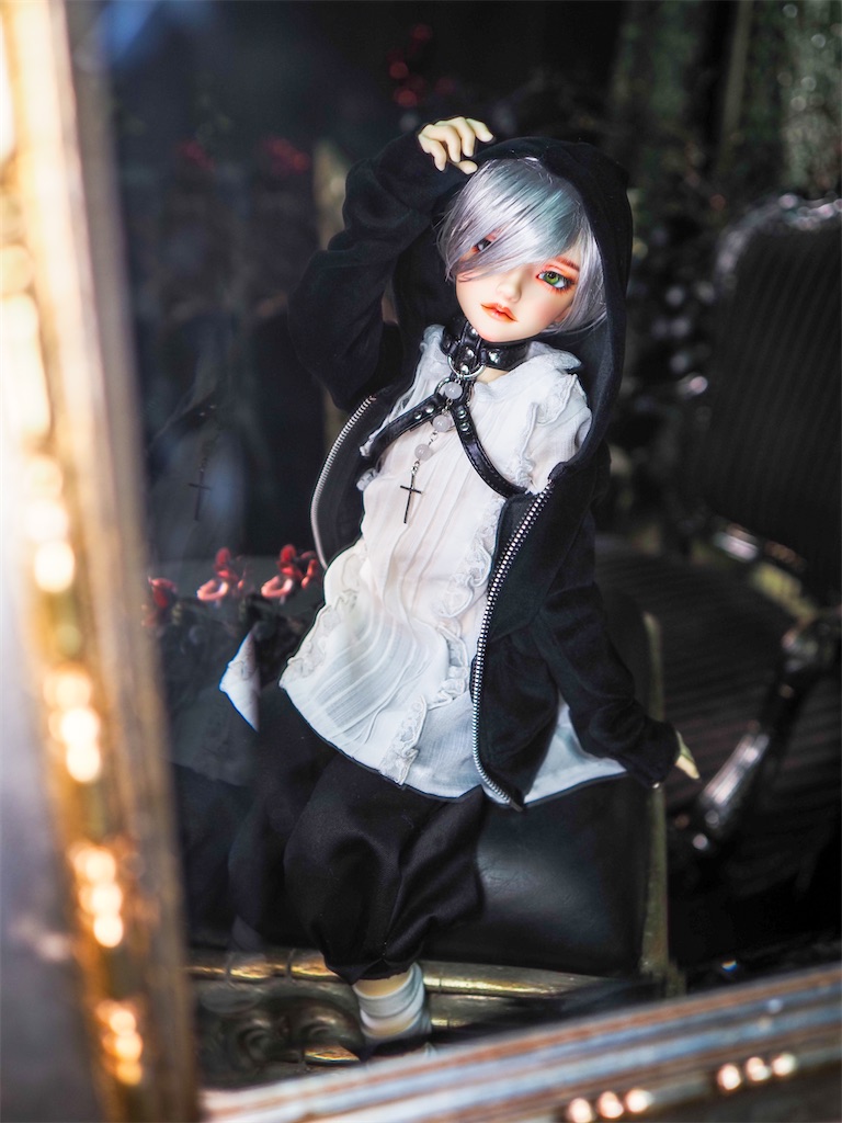 クラシカルな白のブラウスに黒のパンツを着て、黒いパーカーと本革のチョーカーを合わせたつかさくんの写真。