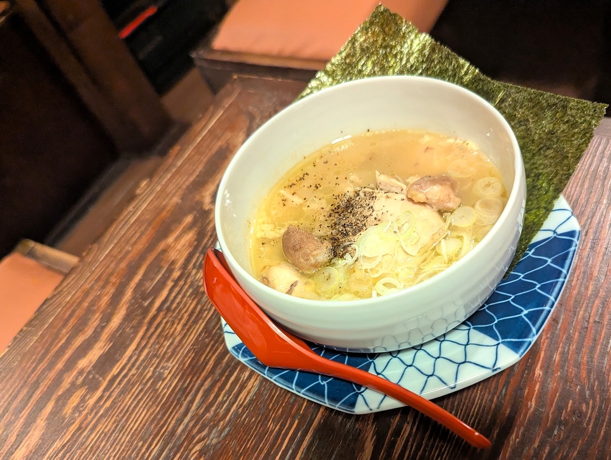 焼鳥どん豊田店の名物「鶏煮込み」599円。鶏もも肉が丸ごと一枚入り、スープに旨味が染みた人気メニュー。黒胡椒とネギ、海苔がトッピングされた、豊田駅近くの焼鳥どんの看板料理の写真。