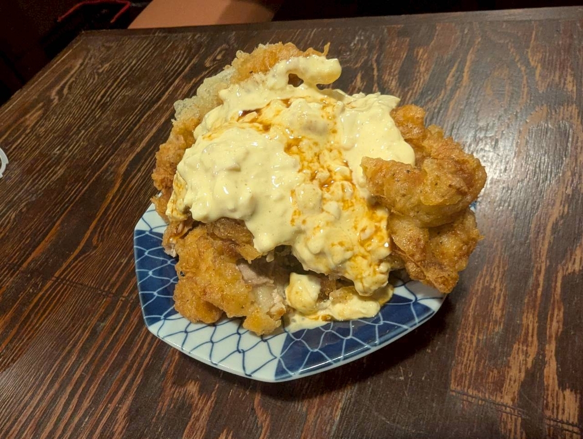 豊田駅の人気焼鳥店『焼鳥どん豊田店』名物、大判の鶏もも肉をカリッと揚げ、自家製タルタルソースを豪快にのせた『タルタルチキン』のアップ写真。衣はザクザク、中は肉汁ジューシーでボリューム満点。甘酸っぱいタルタルがたっぷり絡み、居酒屋定番メニューとして人気のチキン南蛮風一品。