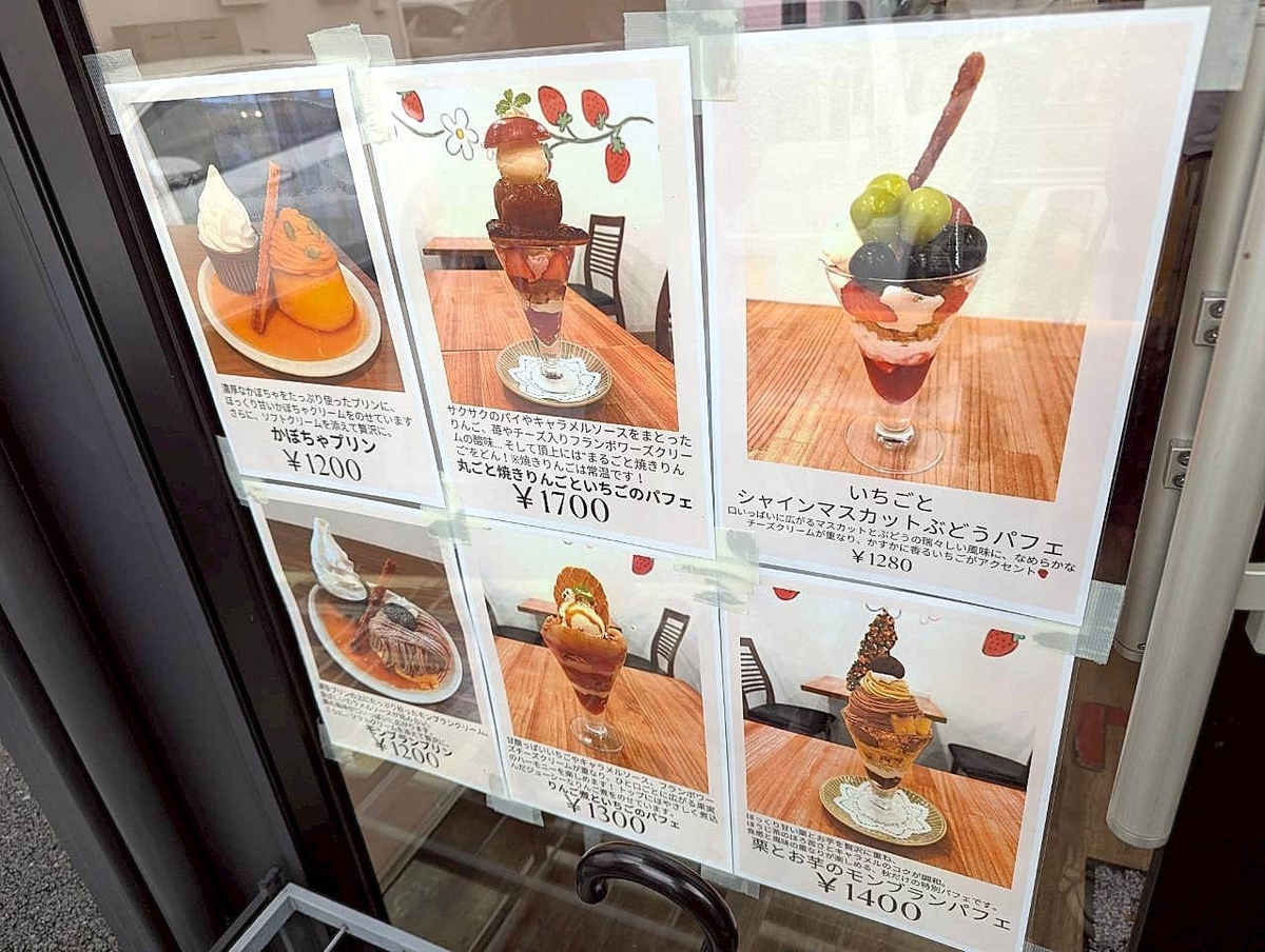 東京いちごカフェの店舗入口に掲示されたスイーツメニュー。栗とお芋のモンブランパフェ（1,400円）や丸ごと焼きりんごといちごのパフェ（1,700円）など、季節限定パフェやプリンが並ぶ。