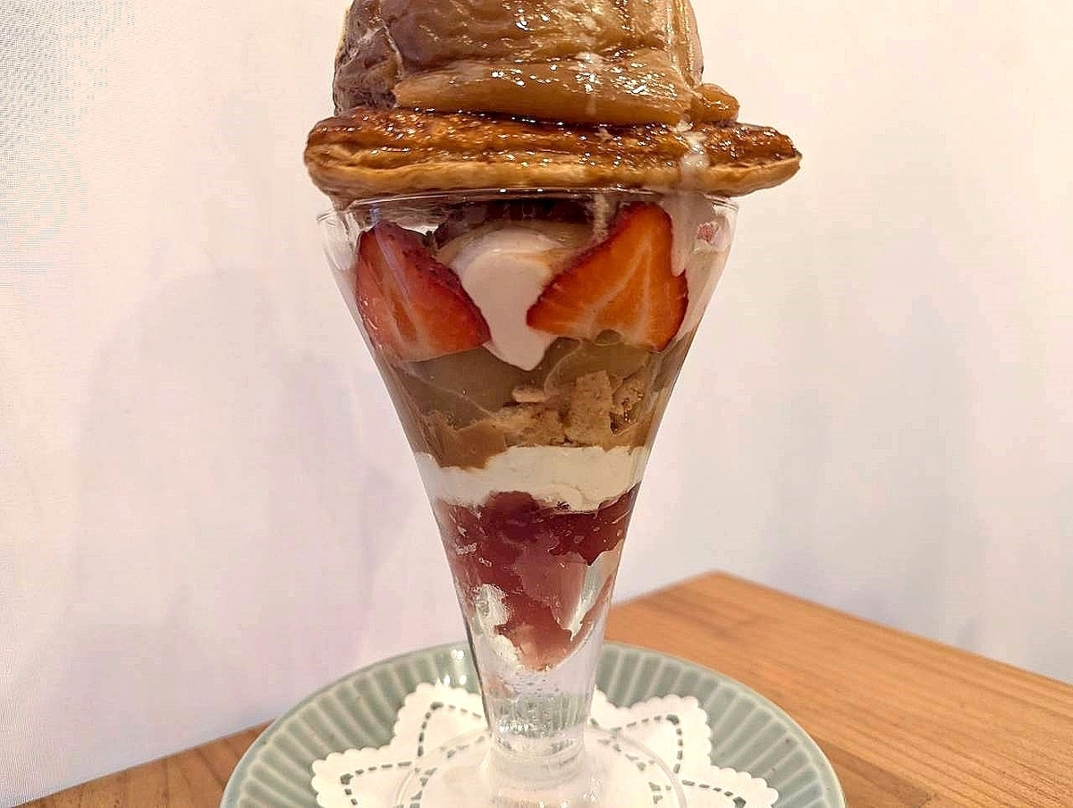丸ごと焼きりんごといちごのパフェの断面。いちご、パイ、キャラメルソース、クリームが層状になっている。