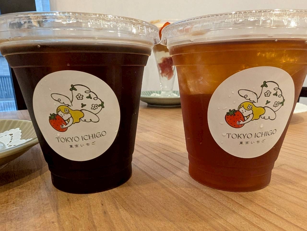 東京いちごカフェのドリンク。左がアイスコーヒー、右がアイスティー。カップにはいちごを持った天使のロゴシールが貼られている。