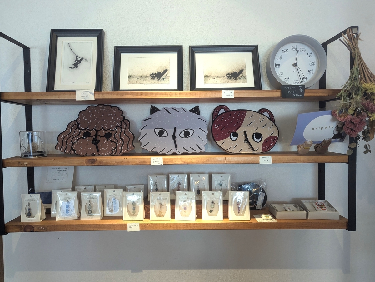 猫目堂茶店の店内に並ぶ猫モチーフの雑貨とアート作品。猫の時計やイラストが飾られた棚の様子