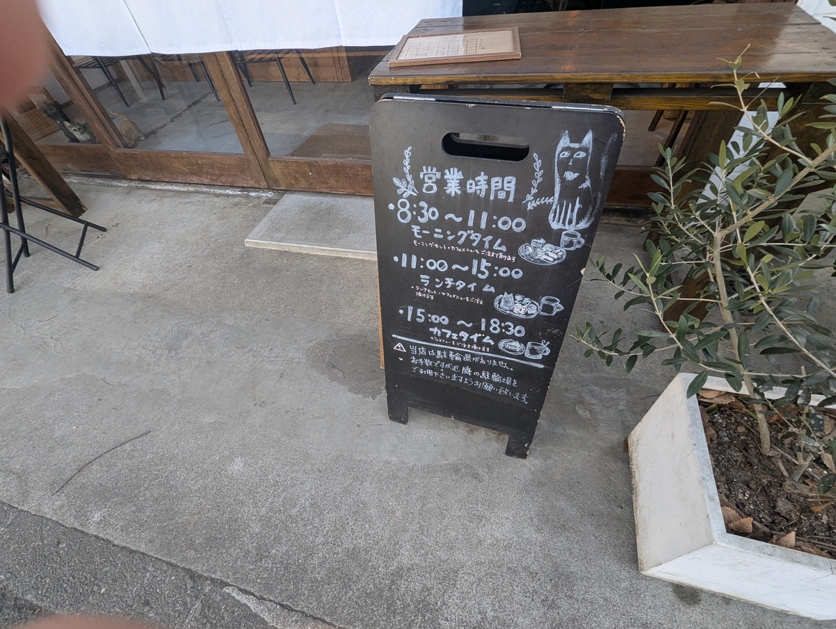 猫目堂茶店の店先に設置された立て看板。モーニング、ランチ、カフェタイムの営業時間が時間帯別に記載されている