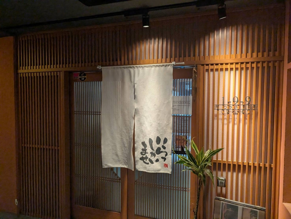 吉祥寺じぞうビル2階にある焼肉 肉つかさの入口。木の格子戸と「いらっしゃいませ」の暖簾が迎える