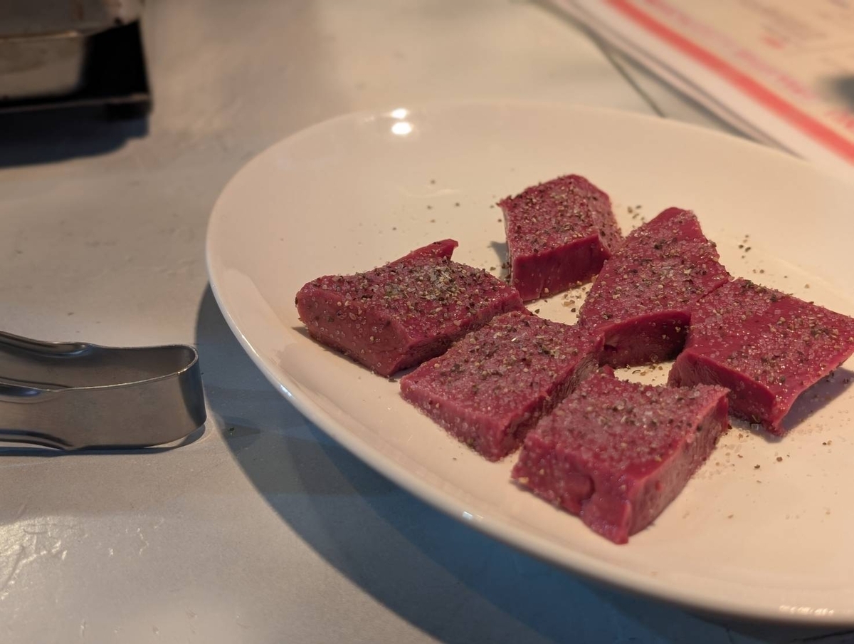 肉つかさの黒毛和牛ハツ。厚切りにカットされた鮮やかな赤紫色のハツに粗挽き胡椒がまぶされ、白い皿に盛られている