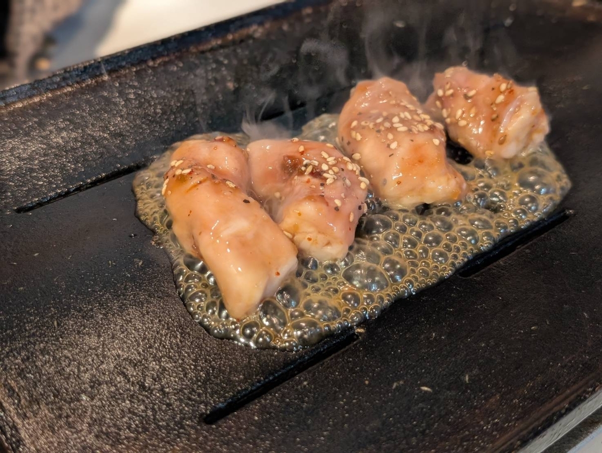 黒毛和牛丸腸を鉄板で焼いている様子。特製たれが泡立ち、表面にごまがまぶされた丸腸から湯気が立ち上っている