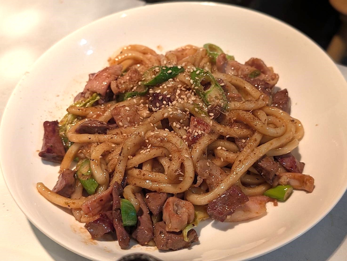 特製ホルモン焼うどん。太めのうどんにホルモンやネギが絡み、ごまが散らされて照りのあるたれで仕上げられている