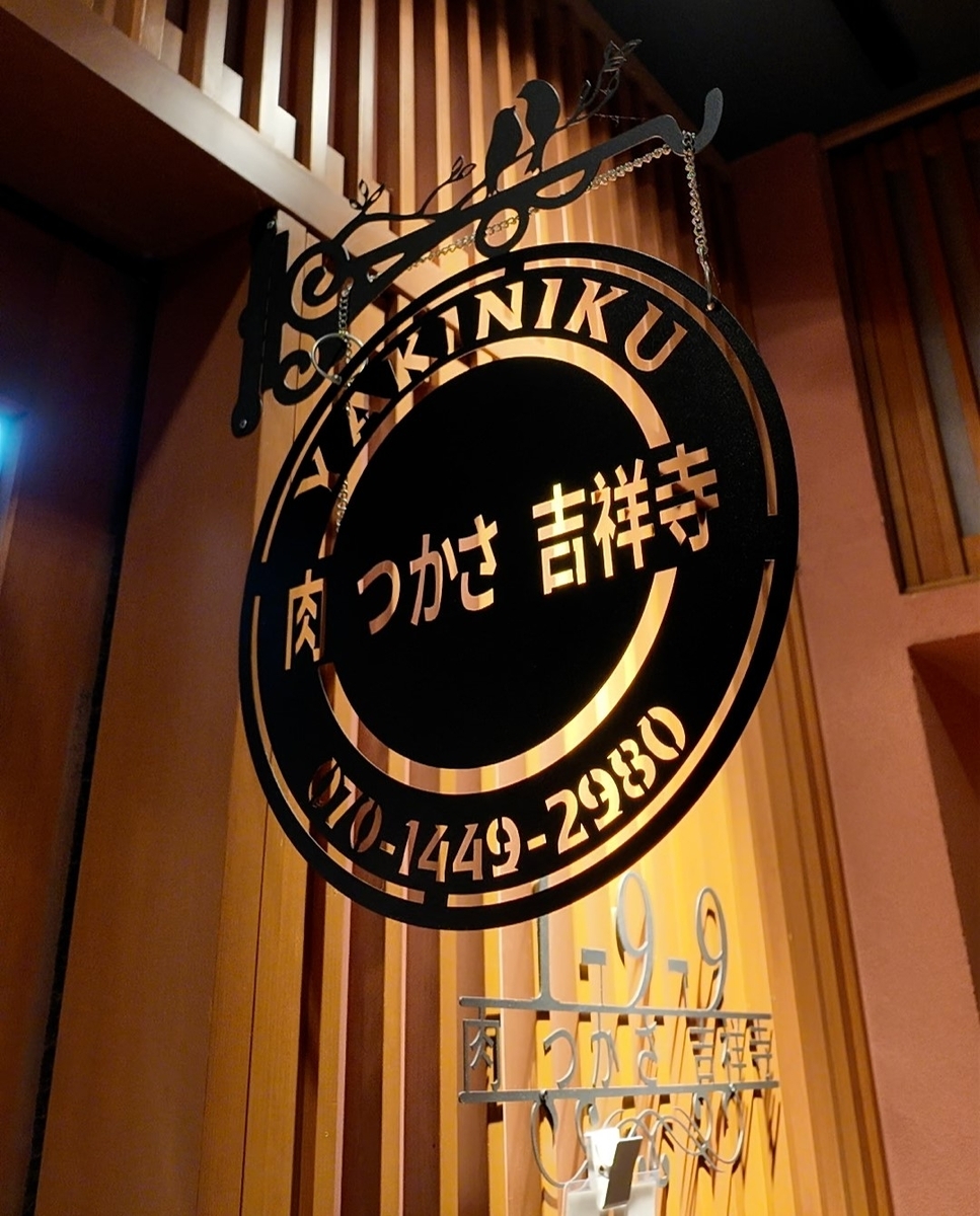焼肉 肉つかさ吉祥寺の看板。黒いアイアン製の丸い看板に「YAKINIKU」「肉 つかさ 吉祥寺」「070-1449-2980」の文字と、鳥のシルエット装飾が施されている