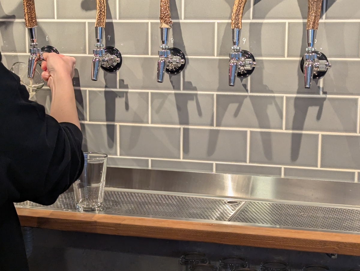 THREE ARROWS BREWINGのビールタップ。タップハンドルに本物の鹿の角が使われており、グレーのタイル壁に5本のタップが並んでいる。スタッフがグラスにビールを注いでいる