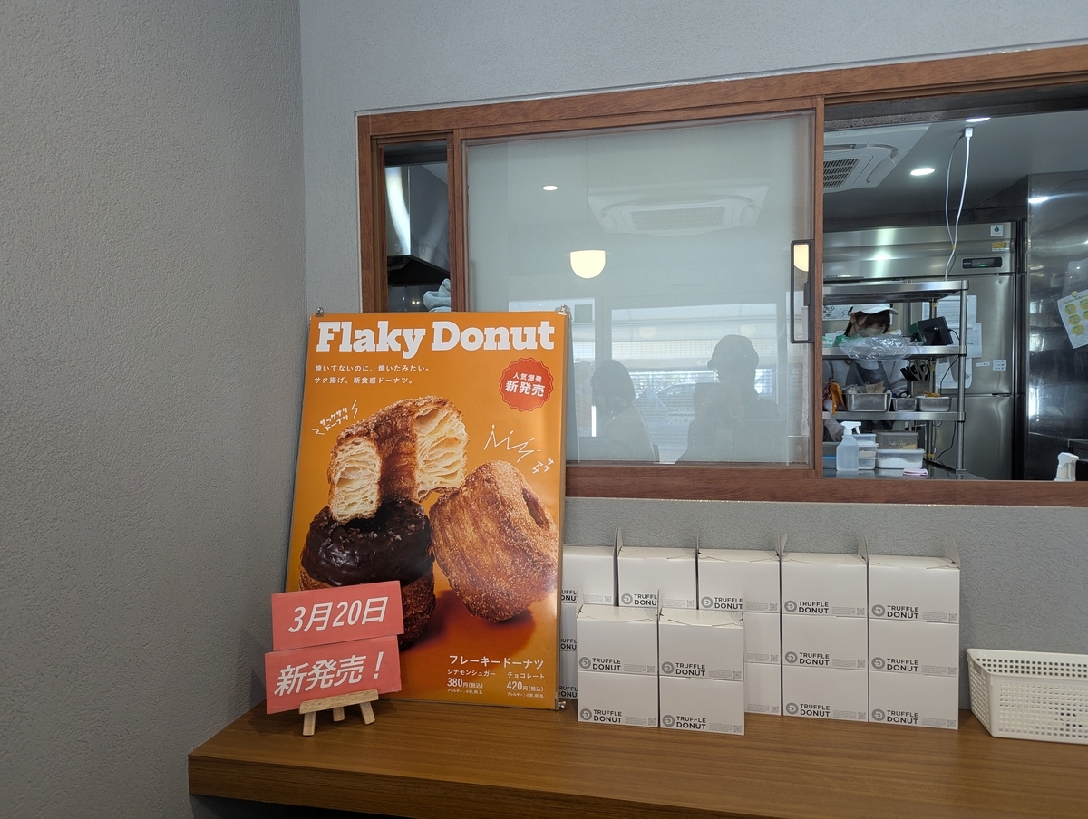 TRUFFLE DONUT店内に掲示されたFlaky Donutの告知ポスター。シナモンシュガーとチョコレートの2種類が写り、「焼いてないのに、焼いたみたい。サク揚げ、新食感ドーナツ。」のコピーと3月20日新発売の案内が添えられている