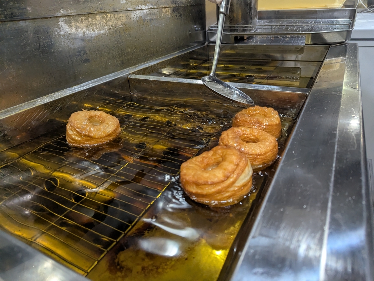 フライヤーの中で揚がるフレーキードーナツ3個。生地が膨らみ、層の隙間が開いてきている