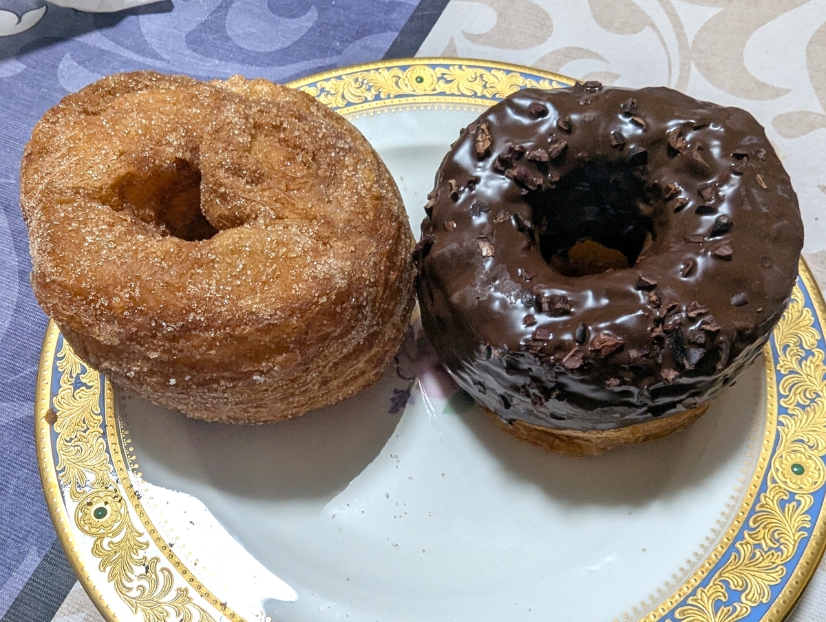 フレーキードーナツのシナモンシュガー（左）とチョコレート（右）を皿に並べた外観。シナモンシュガーは表面にグラニュー糖がきらめき、チョコレートはたっぷりのチョコとカカオニブで覆われている