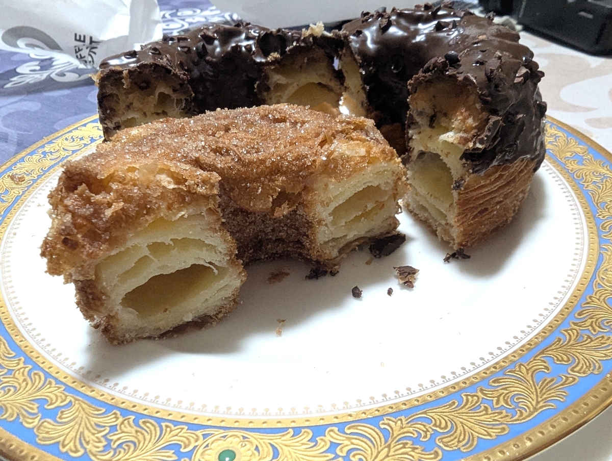 フレーキードーナツのシナモンシュガーとチョコレートを半分に割って皿に並べた断面。どちらも何層にも重なったパイ状の生地が見える