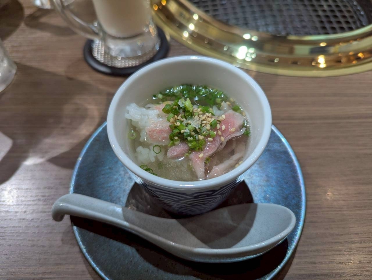 Beef Bossの〆の和牛茶漬け。和牛出汁にネギと白胡麻がかかり、ピンク色の和牛が覗く。蕎麦猪口風の器にレンゲが添えられている