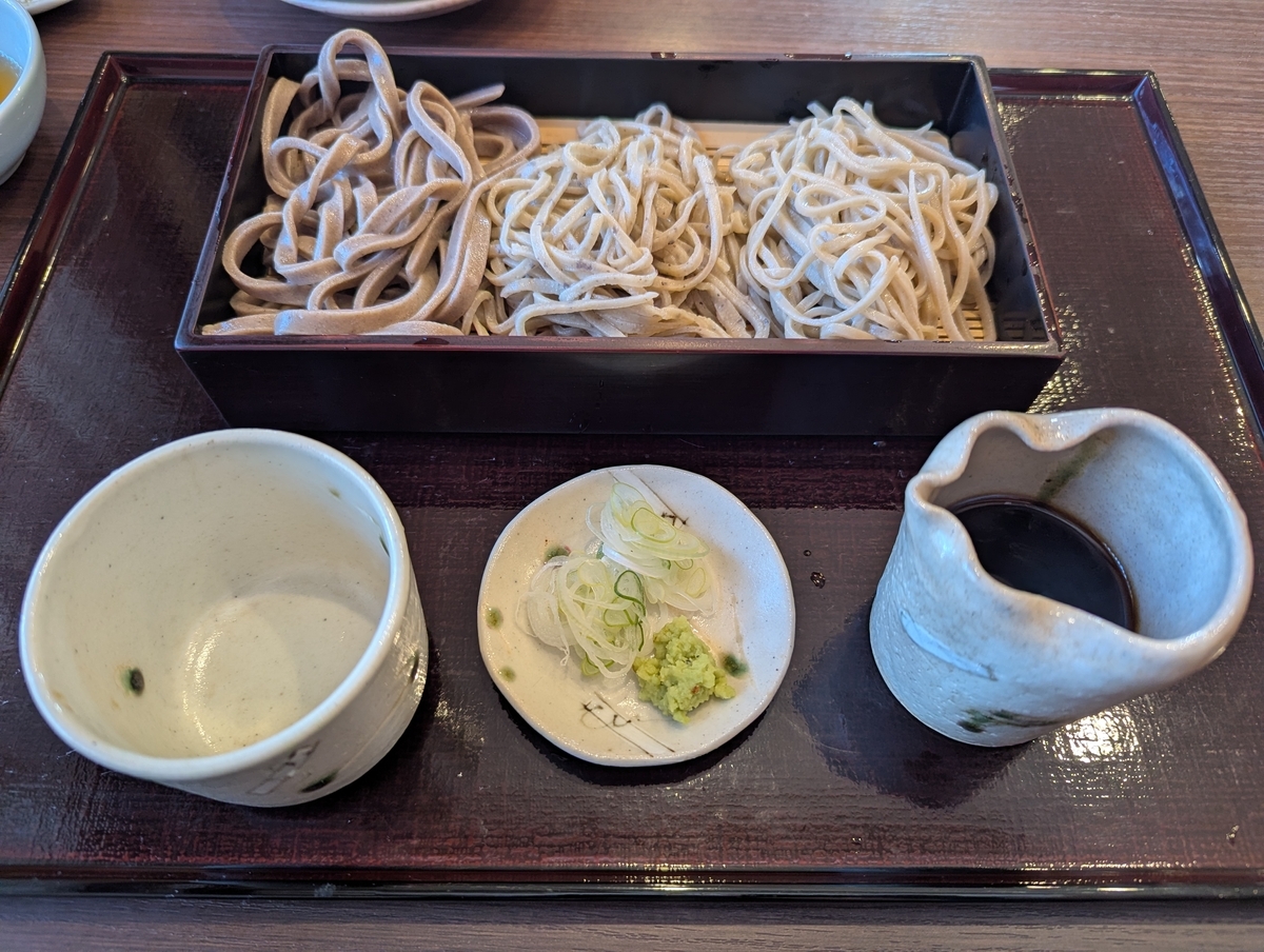 立川たかやの三種食べ比べ。一段の蒸籠に「田舎・粗挽き・せいろ」の三種類の蕎麦が並び、手前に蕎麦猪口、薬味皿(刻みネギ・本わさび)、つゆ徳利が配される